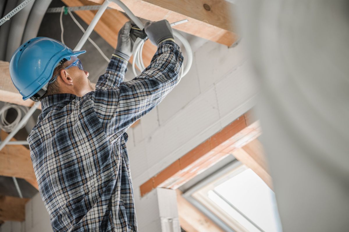 Electrician in a hard hat running cable through ceiling framing in a house under construction