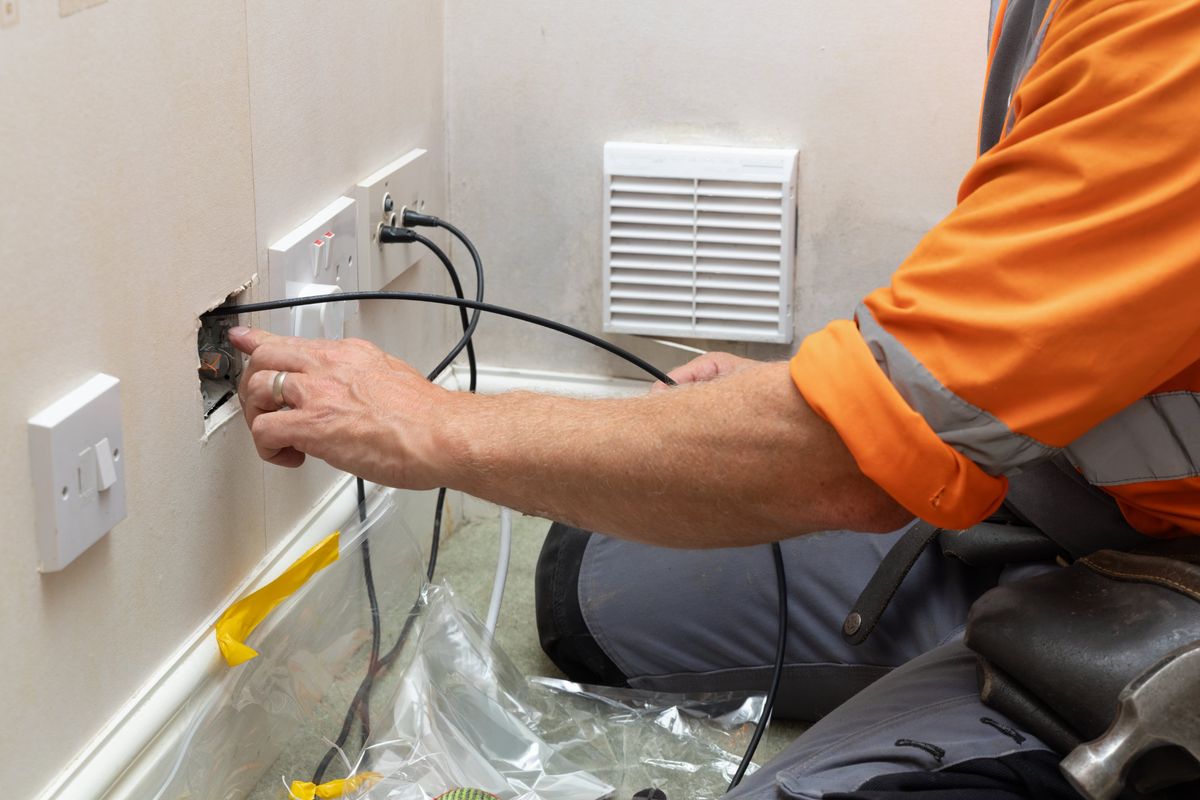 Electrician pulling new cable through an opened wall box beside existing outlets