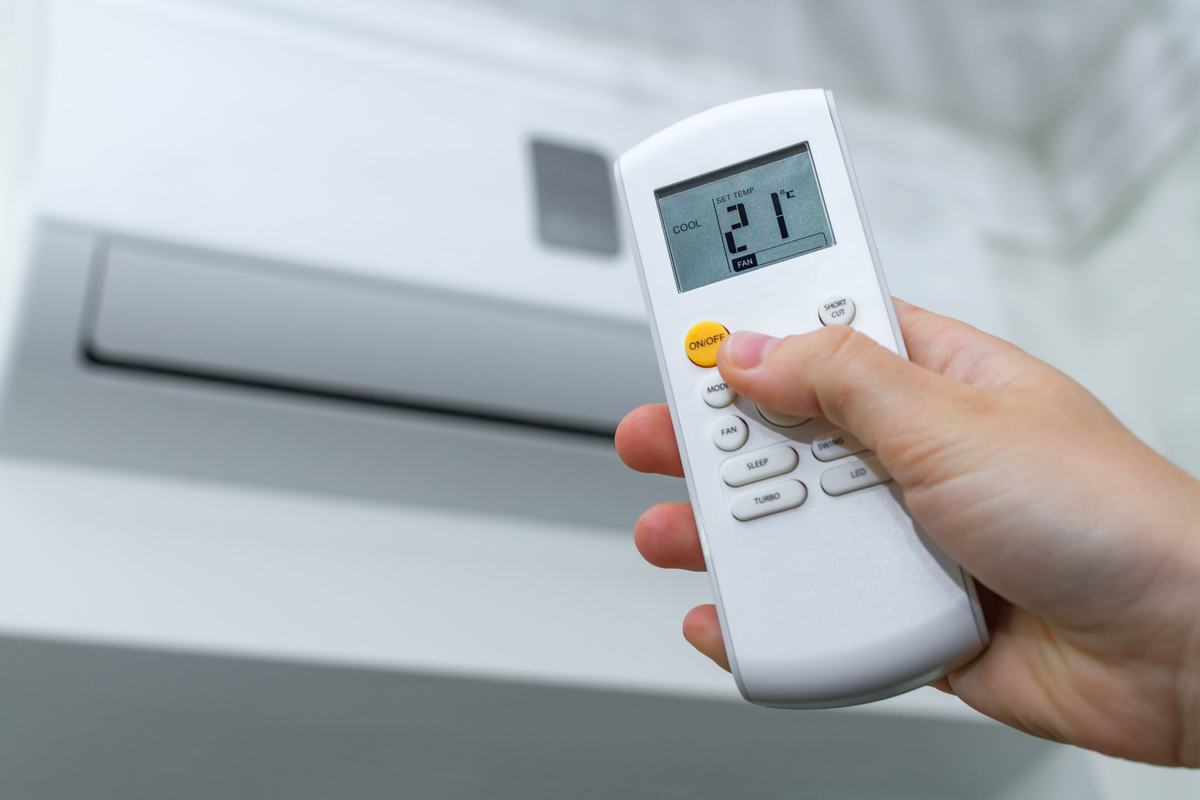 Hand pointing a remote control set to cool at a wall-mounted ductless mini-split unit