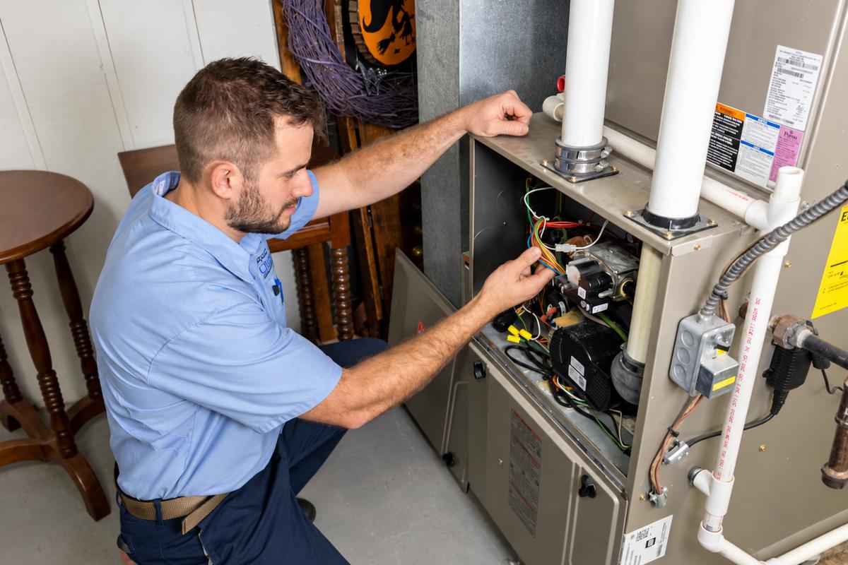 Technician working inside an open gas furnace in a basement